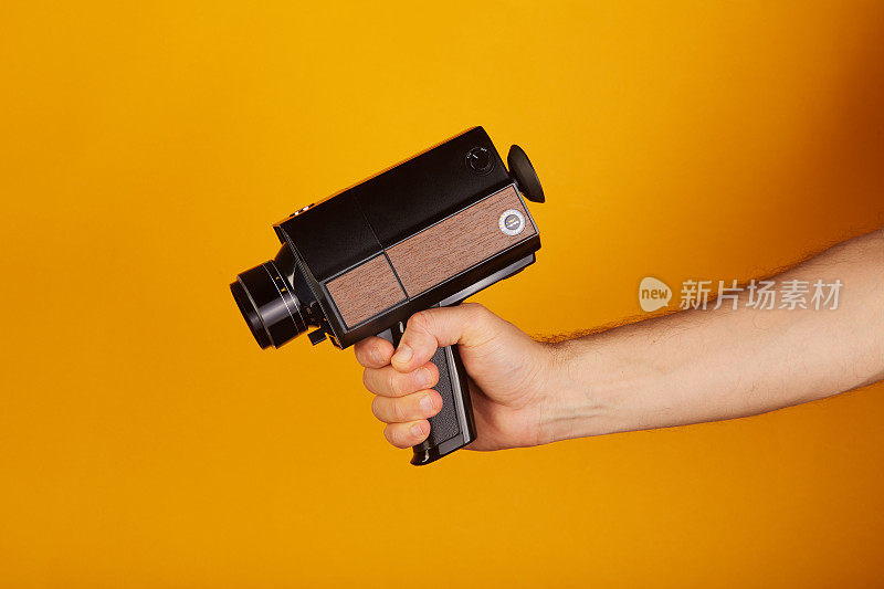 电影摄影师拿着老式模拟Super8, 8毫米电影摄影机在黄色背景。把相机对准枪